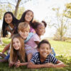 Multi-ethnic group of kids lying on each other in a park Caring for Children