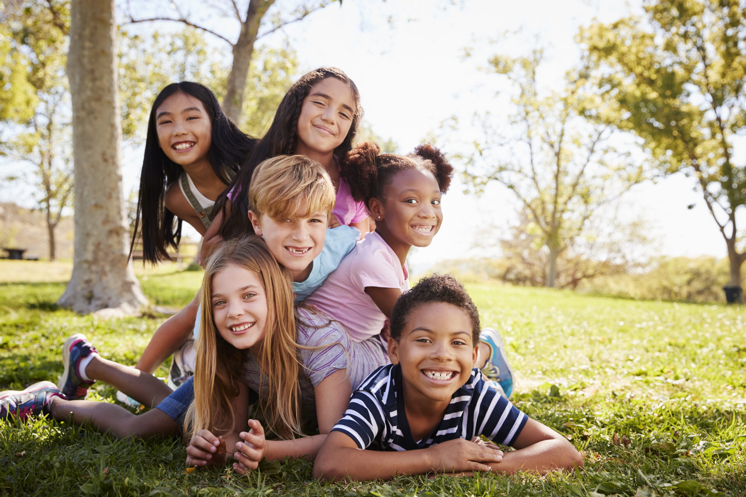 Multi-ethnic group of kids lying on each other in a park Caring for Children
